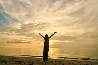 Silhouette of woman with raised arms on beach at sunset