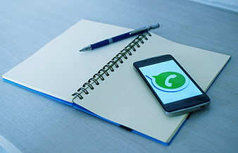 Smartphone with WhatsApp logo on notebook and pen