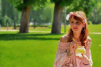 Woman with red hair drinking lemonade in a sunny park