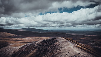 Lone Hiker on Rugged Mountain Ridge Under Dramatic Clouds