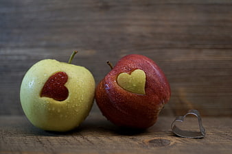 Two Apples with Heart Shapes Cut Out on Wooden Background
