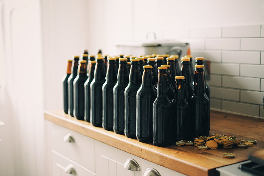 Rows of dark beer bottles on a wooden kitchen counter