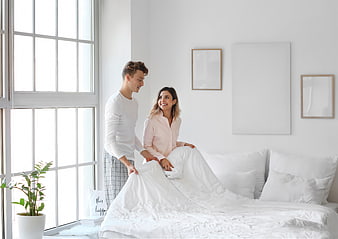 Happy young couple making bed in bright white bedroom