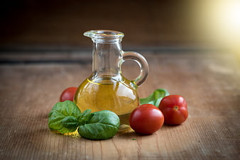 Glass cruet of olive oil with fresh tomatoes and basil on a wooden table