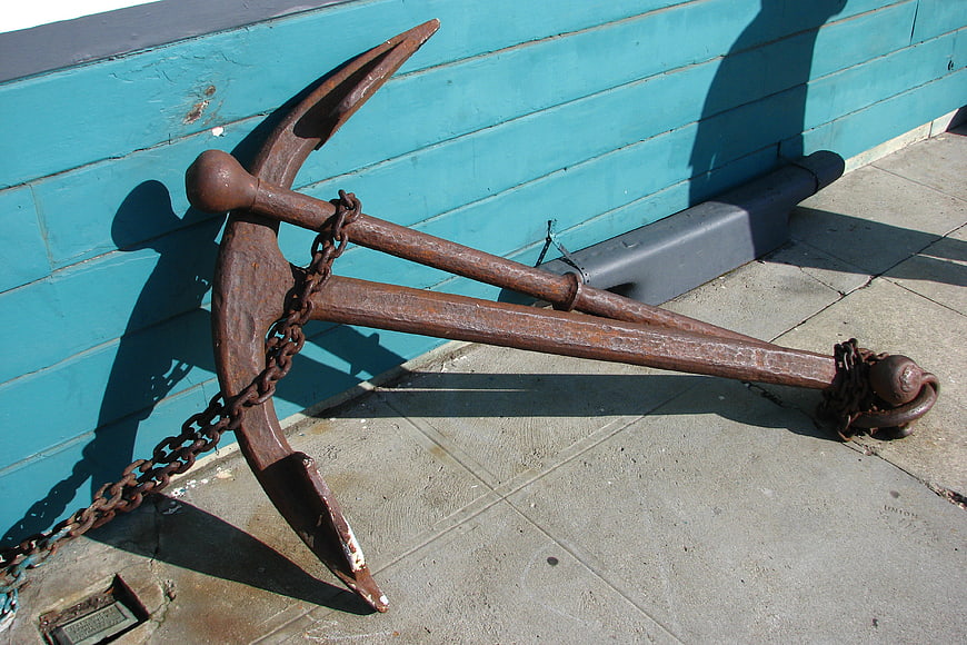 Rusty metal anchor with chain against blue wooden wall
