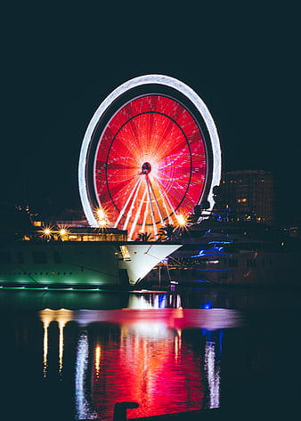 Illuminated Ferris Wheel at Night with Yacht Reflections