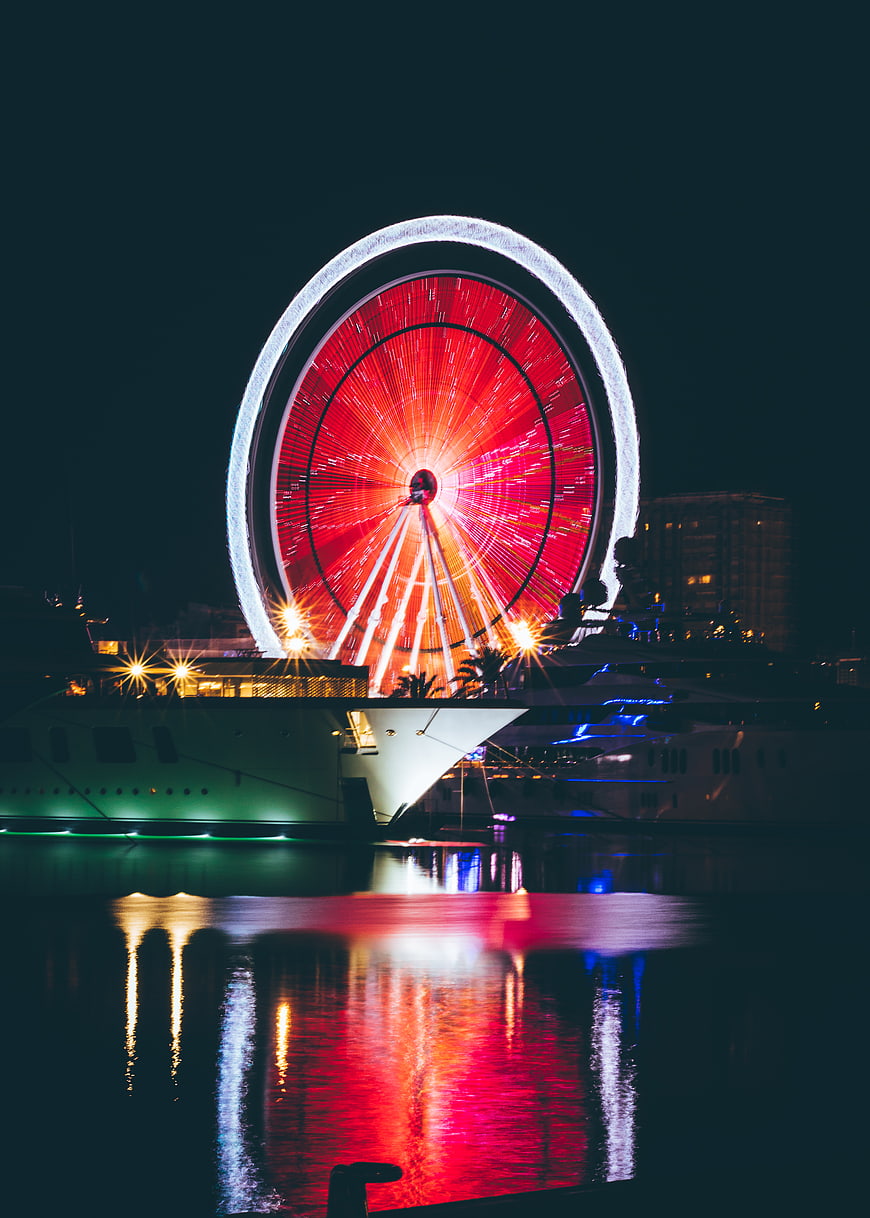 Illuminated Ferris Wheel at Night with Yacht Reflections