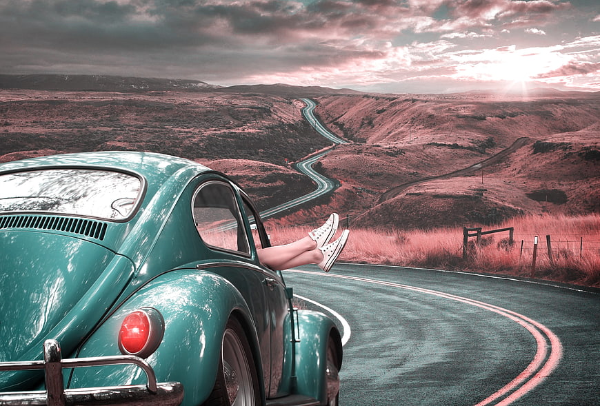 Vintage teal car on winding mountain road with woman's legs out window