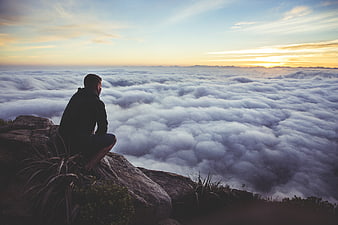 Man sitting on mountain peak overlooking sea of clouds at sunset