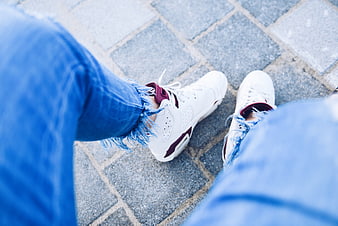 First-person view of white sneakers and ripped blue jeans on pavement