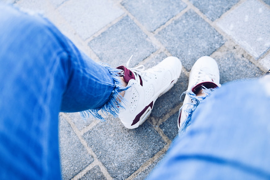 First-person view of white sneakers and ripped blue jeans on pavement