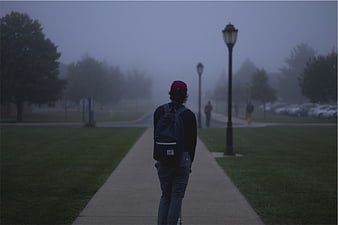 Student walking on foggy campus path with backpack