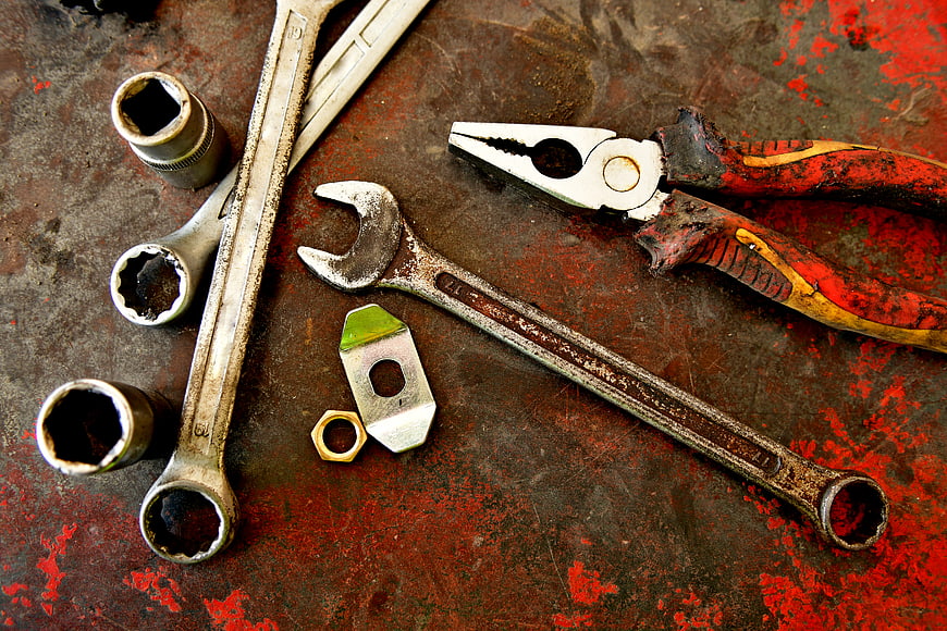 Rusty wrenches and pliers on a worn red metal workbench