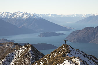 Hiker standing on snowy mountain ridge overlooking lake and peaks