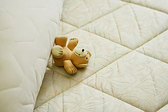 Cute teddy bear lying on a quilted mattress