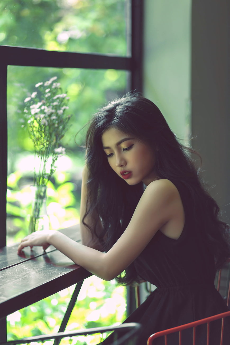 Pensive young woman sitting by window with flowers