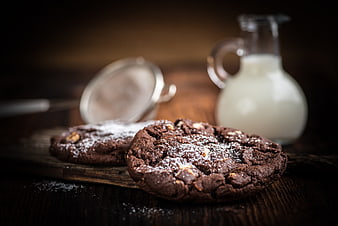 Chocolate cookies with powdered sugar and milk on rustic wood