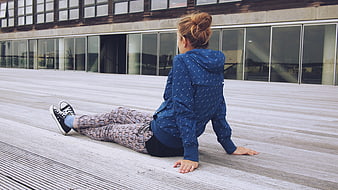 Young woman sitting on wooden deck in blue jacket and patterned pants