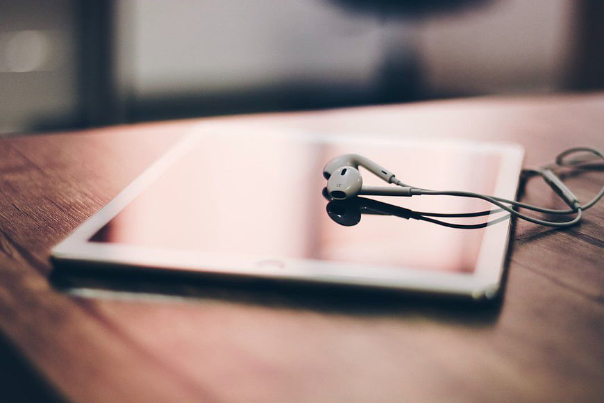 White Earphones on Tablet Screen on Wooden Desk