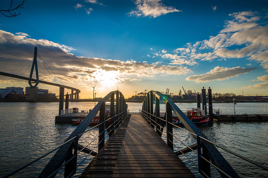 Wooden Pier Leading to Harbor at Sunset with Bridge