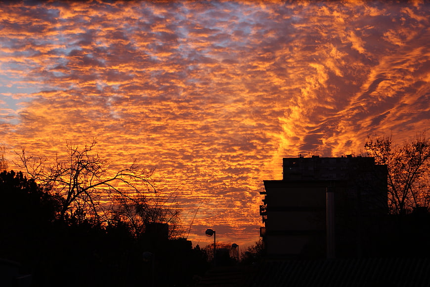 Dramatic orange sunset sky with textured clouds over city silhouette