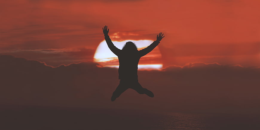 Silhouette of person jumping against dramatic red sunset sky