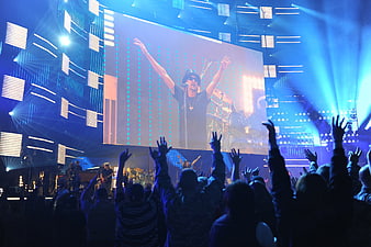 Concert audience with raised hands watching performer on large LED screen