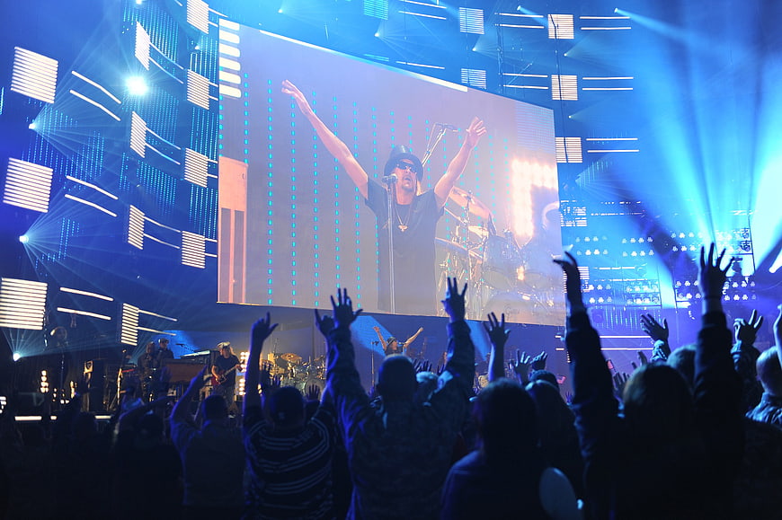 Concert audience with raised hands watching performer on large LED screen