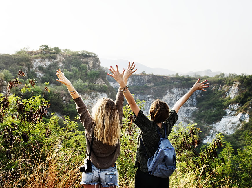 Two female hikers raising arms in joy overlooking scenic canyon