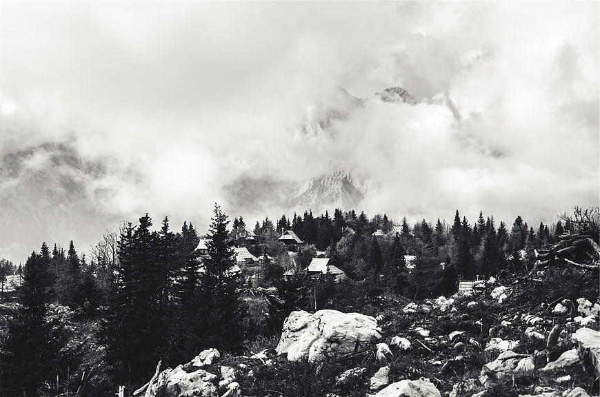Black and white mountain village with clouds and pine trees