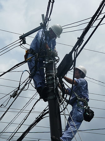 Two electricians repairing overhead power lines on a utility pole