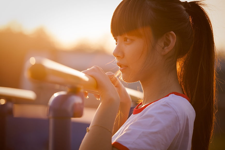 Asian girl leaning on railing at sunset