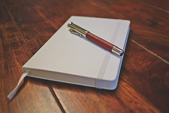 White Notebook and Red Pen on Wooden Table
