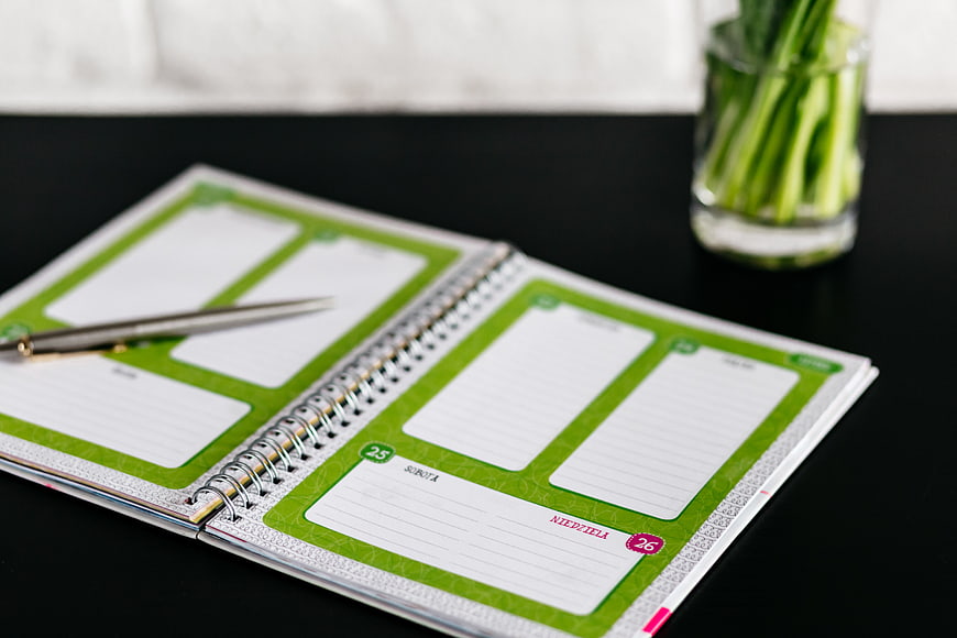 Open Green Planner on Black Desk with Pen and Plant