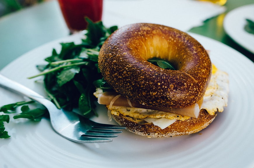 Delicious Bagel Sandwich with Eggs and Ham on White Plate