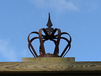Rusty metal crown sculpture on wooden beam against blue sky
