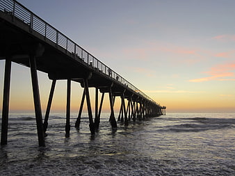Silhouette of long pier extending into ocean at sunset