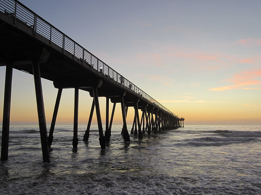 Silhouette of long pier extending into ocean at sunset