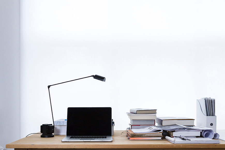 Minimalist office desk with laptop, lamp, and books on white background