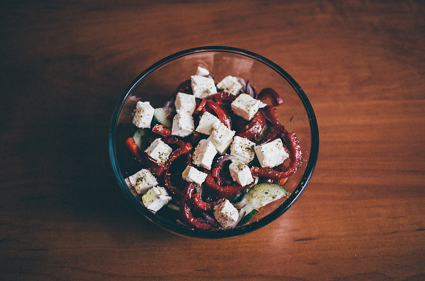 Overhead shot of fresh vegetable salad with feta cheese in glass bowl