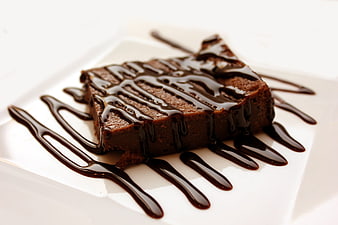 Square chocolate brownie with chocolate drizzle on white plate