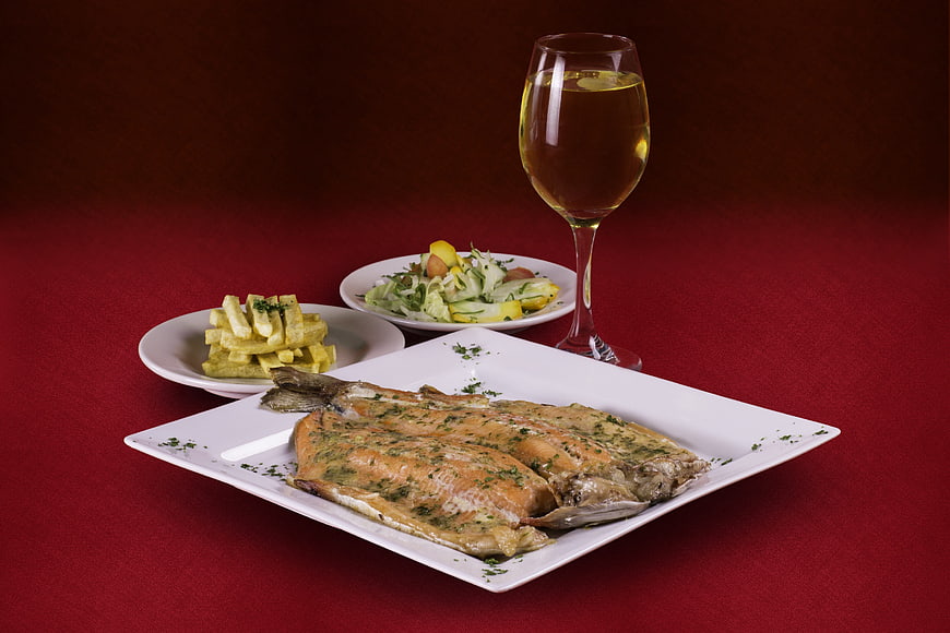 Grilled salmon fillet with fries, salad, and white wine on red background