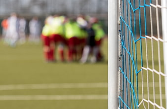 Soccer Goal Net Close-Up With Blurred Team Huddle On Pitch