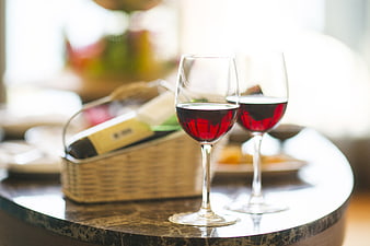 Two glasses of red wine on a marble table with a wine bottle in a basket