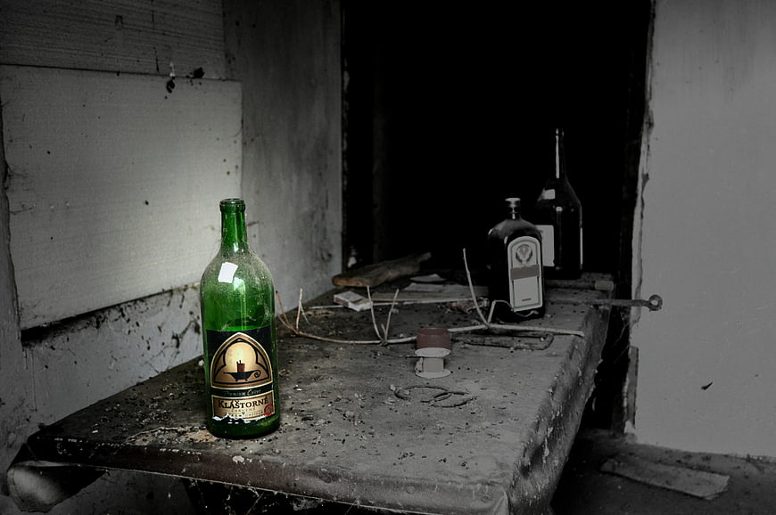 Abandoned green wine bottle on dusty table in dark room