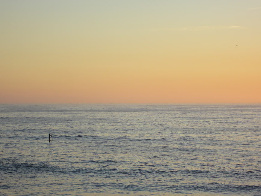 Lone Paddleboarder on Calm Ocean at Sunset