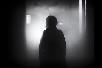 Silhouette of a person standing in a dark, foggy hallway