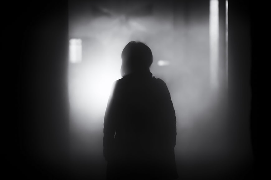 Silhouette of a person standing in a dark, foggy hallway