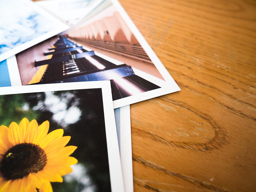 Stack of printed photos on wooden desk with sunflower