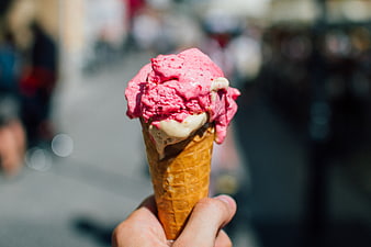 Hand holding pink strawberry ice cream cone outdoors
